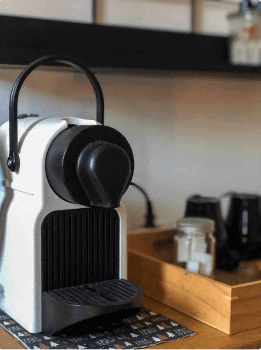 La cafetière Nespresso blanche, avec la bouilloire et les capsules rangées dans un plateau en bois