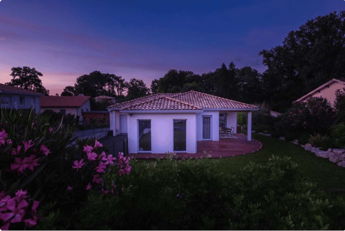 La maison au crépuscule, derrière des fleurs roses au premier plan